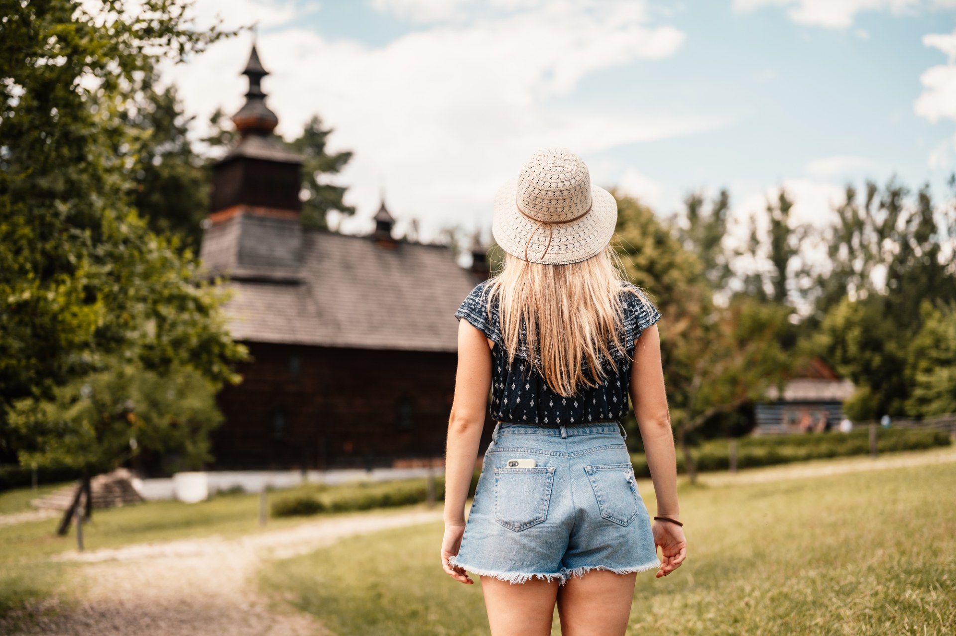 Young woman walking through the open-air folk museum in Stara Lubovna towards a wooden church